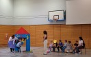 Kinder sitzen auf der Bank. Ein Schüler geht durch die Tür einer selbstgebastelten Schule