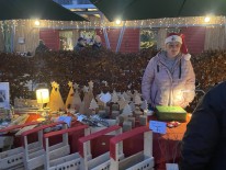 Junge Frau mit Weihnachtsm&uuml;tze steht als Verk&auml;uferin hinter den gebastelten Sachen