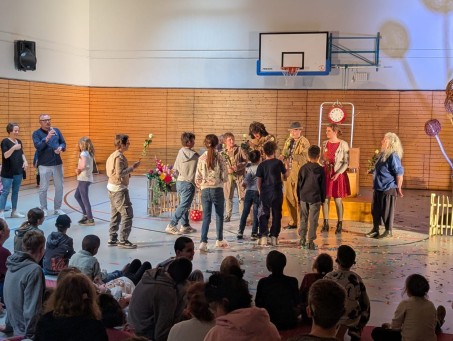 Schüler*innen gehen zur Theatergruppe nach vorne und überreichen Blumen