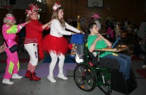 Polonaise vorn Junge im Rollstuhl im gr&uuml;nen Shirt, dahinter 3 Frauen. Davon zwei rot/wei&szlig; verkleidet und eine im Pinken Trainingsanzug.
