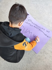 Junge schreibt auf ein lila Plakat: gemeinsam feiern wir Vielfalt und Zusammenhalt